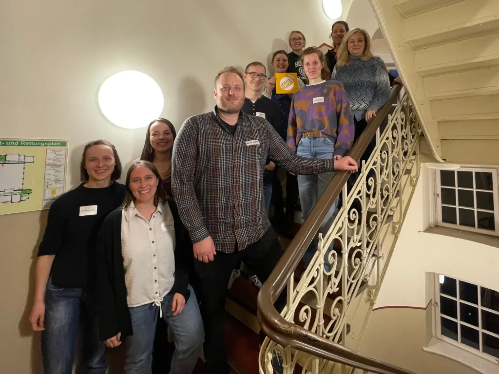 Gruppenfoto von Personen auf einer Treppe, Lächeln und Austausch in einem Innenraum mit Beleuchtung.